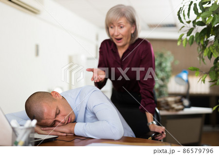 Office employee sleeping at workplace on background of dissatisfied female boss Office employee sleeping at workplace on background of dissatisfied female boss 86579796