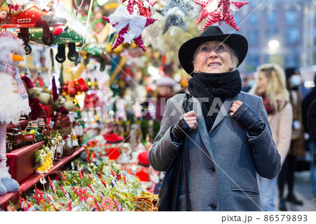 Positive elderly woman in festive mood walking on street Christmas fair 86579893