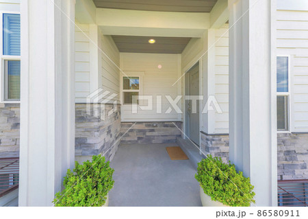 Entrance of a house with gray door on the side and two potted plants near the column posts 86580911