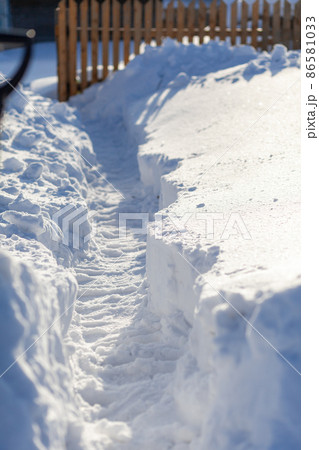 A man dug a passage through a lot of snow. Clearing snow to the house and fence after a big snowfall in winter. A man dug a passage through a lot of snow. Clearing snow to the house and fence after a big snowfall in winter. 86581033