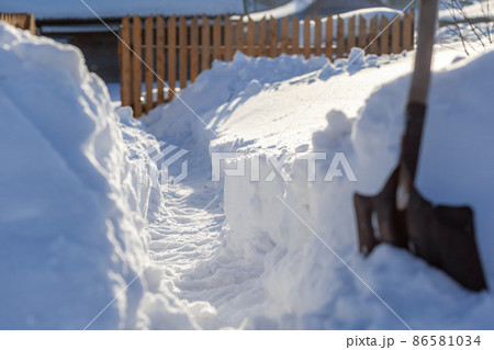 A man dug a passage through a lot of snow. Clearing snow to the house and fence after a big snowfall in winter. A man dug a passage through a lot of snow. Clearing snow to the house and fence after a big snowfall in winter. 86581034