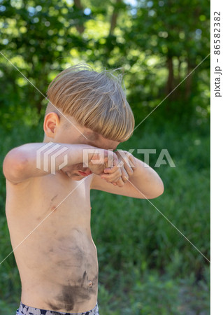 Upset, sad and crying caucasian boy 5 years old with blond hair, stained or dirty. Rubs his eyes. 86582382