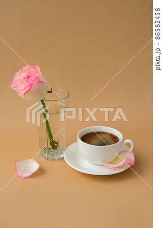 Tender pink rose on vase with white cup of coffee on beige background. Minimal composition. Romantic pastel pink rose flower. Modern aesthetic. Neutral earth tones. Holiday morning breakfast Tender pink rose on vase with white cup of coffee on beige background. Minimal composition. Romantic pastel pink rose flower. Modern aesthetic. Neutral earth tones. Holiday morning breakfast 86582458