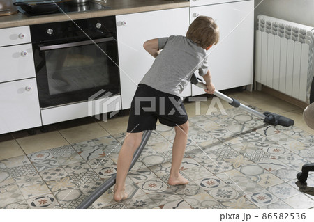 6-year-old boy is cleaning house, vacuuming kitchen floor 6-year-old boy is cleaning house, vacuuming kitchen floor 86582536