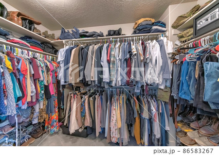 Full walk in closet with clothes hanging on the clothing rods 86583267