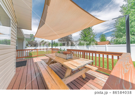 Deck of a house with wooden chairs and table under a shade sail Deck of a house with wooden chairs and table under a shade sail 86584038