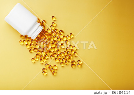 Gold Vitamin D3 capsules poured out of a jar on a yellow background with free space 86584114