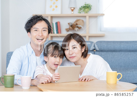 リビングでタブレットを操作する小学生の女の子とパパとママのポートレート 86585257