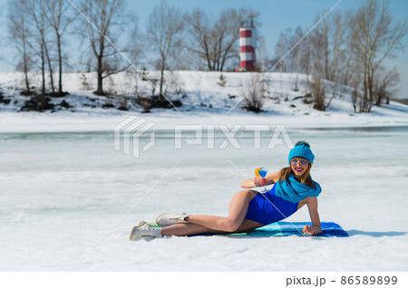 Beautiful caucasian woman in a swimsuit and a hat sunbathes and drinks a cocktail on the snow.  86589899