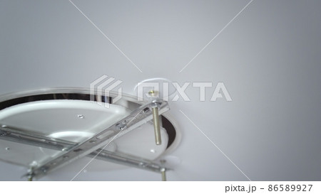 A close-up of the hands of an unrecognizable man inserting the base for mounting a ceiling light. Repair A close-up of the hands of an unrecognizable man inserting the base for mounting a ceiling light. Repair 86589927