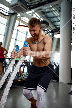 Front view of Attractive young fit and toned sportswoman working out with battle ropes. Motion blur Front view of Attractive young fit and toned sportswoman working out with battle ropes. Motion blur 86591156