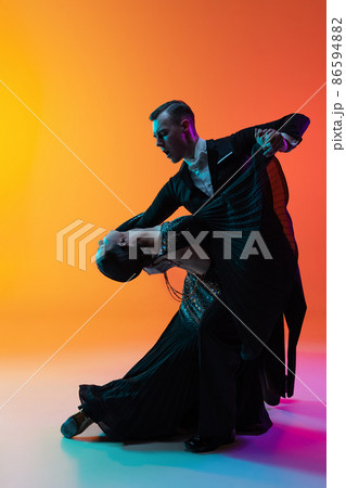 Portrait of young beautiful man and woman dancing ballroom dance isolated over gradient orange pink background in neon light. Beauty, art, sport concept Portrait of young beautiful man and woman dancing ballroom dance isolated over gradient orange pink background in neon light. Beauty, art, sport concept 86594882