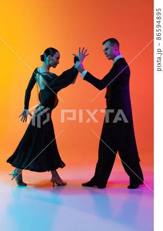 Full-length portrait of young beautiful man and woman dancing ballroom dance isolated over gradient orange pink background in neon light. Beauty, art, sport concept 86594895