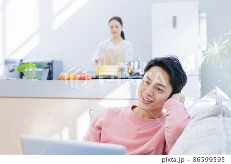自宅でのんびりパソコンに向かう夫と料理をする妻 86599595