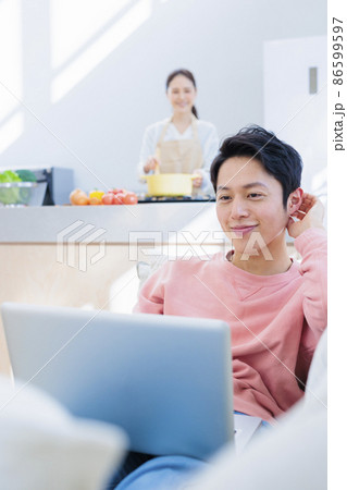 自宅でのんびりパソコンに向かう夫と料理をする妻 86599597