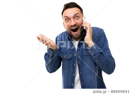 Surprisedly charismatic man with open mouth and wide eyes speaks on the phone gesturing with his 86600691