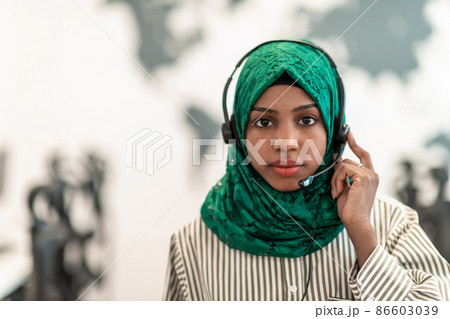 Afro Muslim female with green hijab scarf customer representative business woman with phone headset helping and supporting online with customer in modern call centre Afro Muslim female with green hijab scarf customer representative business woman with phone headset helping and supporting online with customer in modern call centre 86603039