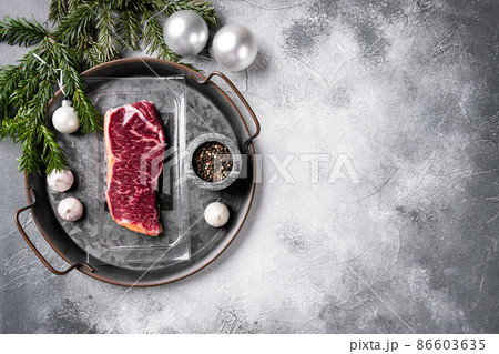 Raw steak with Christmas tree decorations, on gray stone table background, top view flat lay, with copy space for text Raw steak with Christmas tree decorations, on gray stone table background, top view flat lay, with copy space for text 86603635