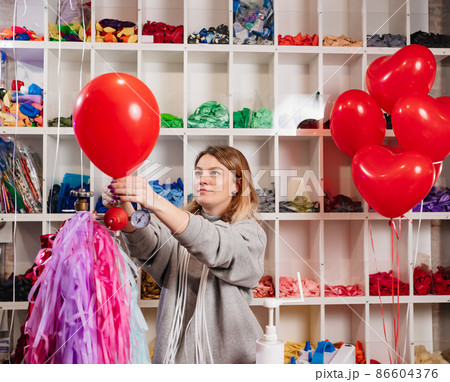 a woman inflates of helium from a red balloon. 86604376