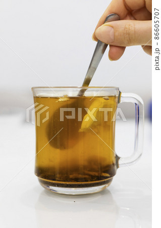 A glass cup of hot tea with honey and lemon on a light background. 86605707