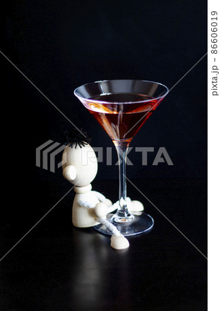 Toy wooden man hugging a martini glass on a black background. The concept of drunkenness, alcoholism. vertical photo 86606019