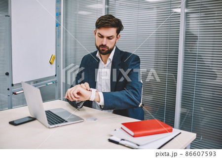 Serious businessman looking at wristwatch while working in office Serious businessman looking at wristwatch while working in office 86607593