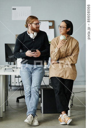 Two young intercultural businessmen in casual clothes standing by desk Two young intercultural businessmen in casual clothes standing by desk 86608066