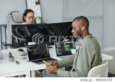 Young African American office worker in earphones scrolling in mobile phone Young African American office worker in earphones scrolling in mobile phone 86608193