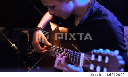 Man plays guitar. Young man plays a musical instrument. Musician records his composition in a music Studio using professional microphone 86610002