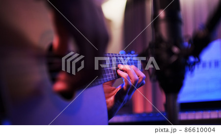 Close-up of the hands of a musician playing an acoustic guitar. Guitarist records music in the studio. Guitar and recording microphone close-up. 86610004