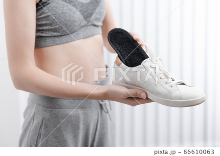 Fitness woman in sportswear with orthopedic insoles and sneakers. Woman putting orthopedic insole into shoe at home close up. Foot care banner. Flat Feet Correction. Fitness woman in sportswear with orthopedic insoles and sneakers. Woman putting orthopedic insole into shoe at home close up. Foot care banner. Flat Feet Correction. 86610063