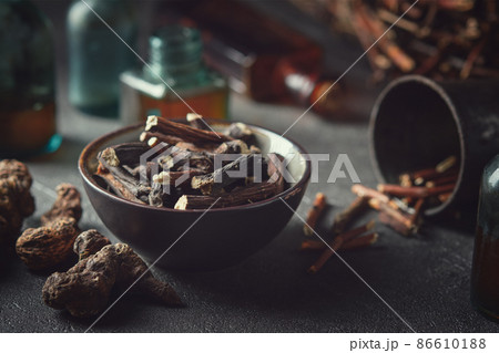 Black bowl of Common comfrey or symphytum officinale roots. Dried comfrey officinalis roots, knitbone and Bistort, Snakeweed. Bottles of infusion and tincture. Alternative herbal medicine. 86610188
