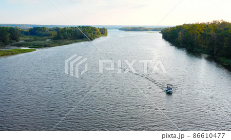 Photo from drone above a river with a slow drifting speedboat while sunset with people on board. Aerial view of driving powerboat on lake in the summer.. Photo from drone above a river with a slow drifting speedboat while sunset with people on board. Aerial view of driving powerboat on lake in the summer.. 86610477