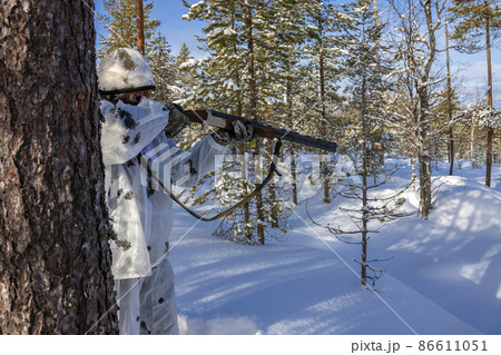 Hunter in winter camouflage with his face covered by mask is preparing to fire gun. Hunter in winter camouflage with his face covered by mask is preparing to fire gun. 86611051