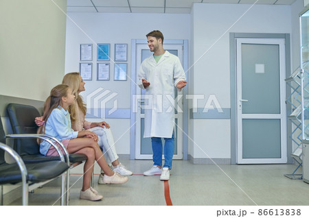 Young male doctor talking to the patients in the clinic hall Young male doctor talking to the patients in the clinic hall 86613838