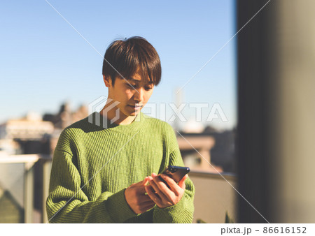 青年は自宅のベランダでスマートフォンを操作している 86616152