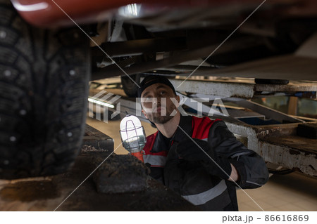 Mechanic Inspecting Car on Lift in Workshop Mechanic Inspecting Car on Lift in Workshop 86616869