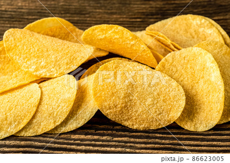 Potato chips on a wooden background. Salty crisps scattered on a table. Potato chips on a wooden background. Salty crisps scattered on a table. 86623005