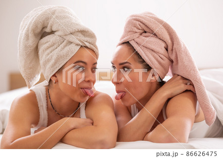 Girls' night for mom and daughter with hair wrapped in towels, sticking their tongues out at each other, having fun 86626475