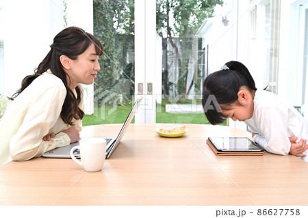 向かい合って仕事をする母親と学習する女の子 86627758