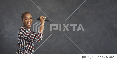 Wow, that's cool. Copy space banner background with studio portrait of happy smiling black woman holding binoculars, waiting and looking forward to big sale, bargain, special offer, clearance, blowout 86628382