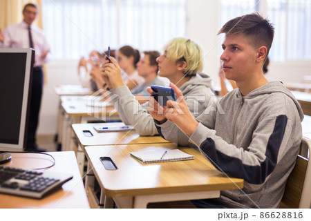 Modern teenagers sitting with mobile phones on lesson 86628816