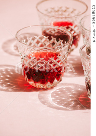 Red wine in a transparent glass with abstract shadows on pink background. Red wine in a transparent glass with abstract shadows on pink background. 86629615