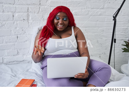 Smiling woman looking at computer while sitting on white bed Smiling woman looking at computer while sitting on white bed 86630273