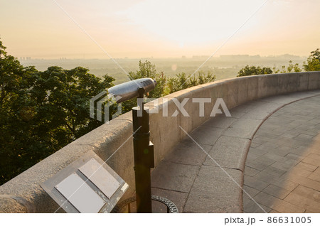 Tourist coin telescope. Metal stationary binoculars standing on a high hill on the viewpoint, for observing the nature of a beautiful old historic city overlooking the river 86631005