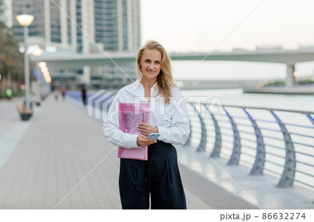 A beautiful business woman with a folder of documents in her hands outdoors. City portrait, business portrait A beautiful business woman with a folder of documents in her hands outdoors. City portrait, business portrait 86632274