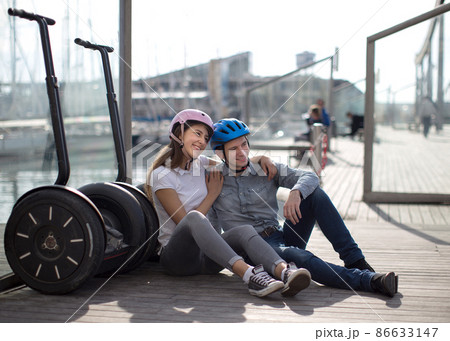 young couple guy and girl are walking on the segway along the board paved promenade in the port of a European city young couple guy and girl are walking on the segway along the board paved promenade in the port of a European city 86633147