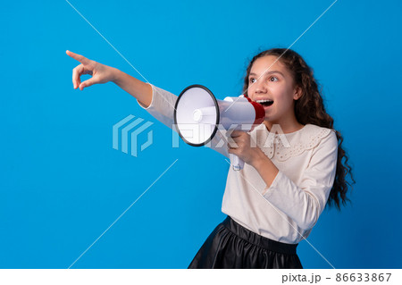 Cute schoolgirl holding megaphone against blue background 86633867
