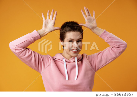 Young woman with short hair doing funny gesture over head as bull horns over yellow background Young woman with short hair doing funny gesture over head as bull horns over yellow background 86633957