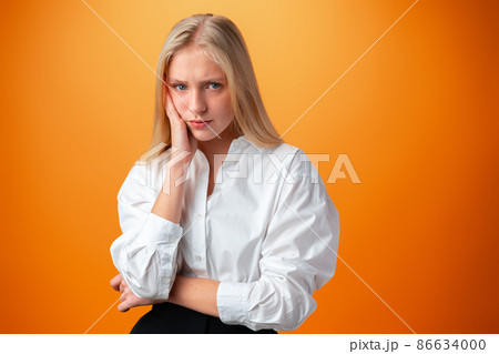 Teen girl is bored and thinking over orange background Teen girl is bored and thinking over orange background 86634000